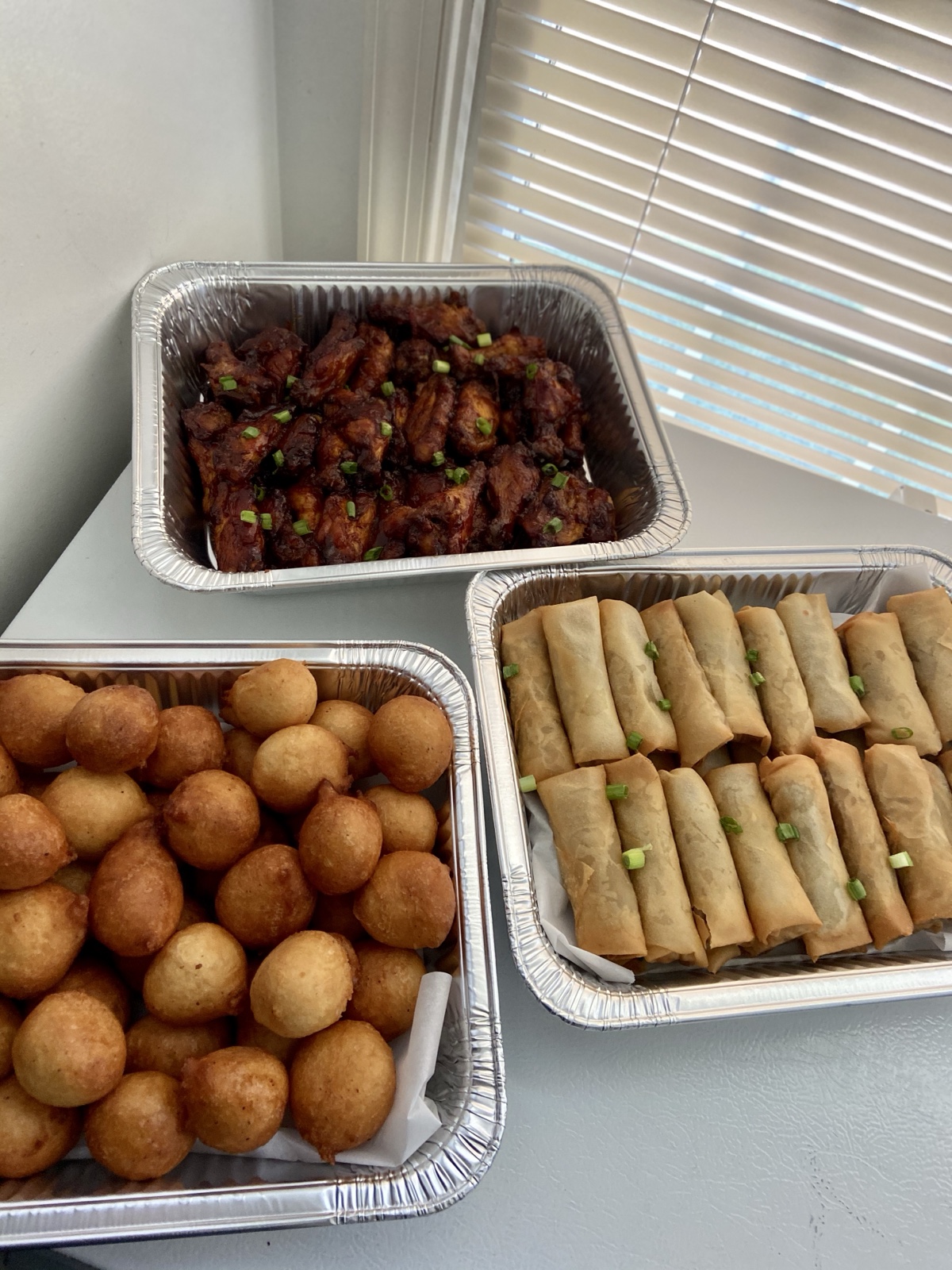 Catering trays of saucy chicken wings, golden puff puff and crispy spring rolls