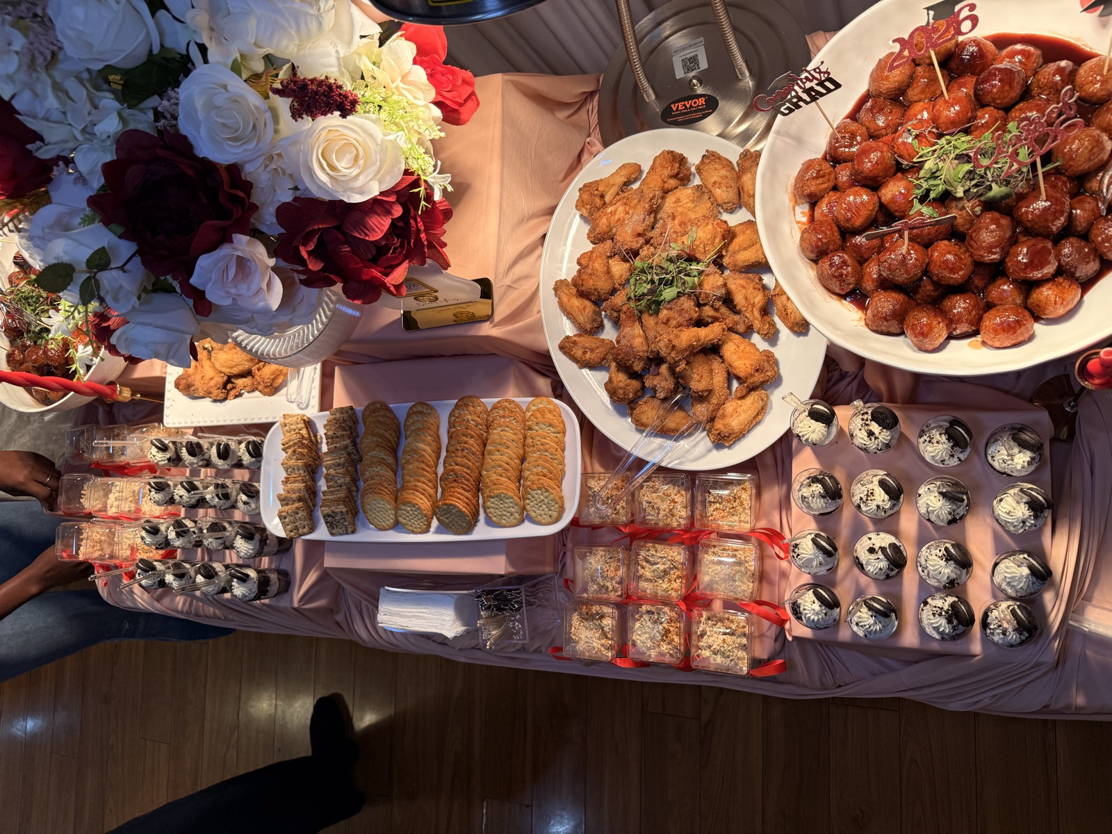 A styled celebration spread with fried chicken, glazed cocktail meatballs, dessert cups and florals on a blush-draped table