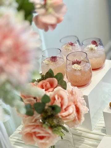 Blush mocktails garnished with edible flowers on a styled display riser with roses
