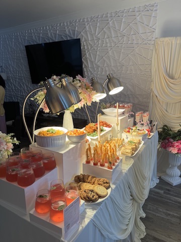 A styled display table of pink mocktails, small chops and florals against a draped backdrop