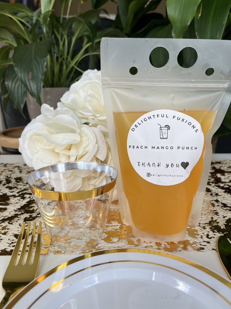 A Delightful Fusions Peach Mango Punch pouch on a gold-trimmed place setting
