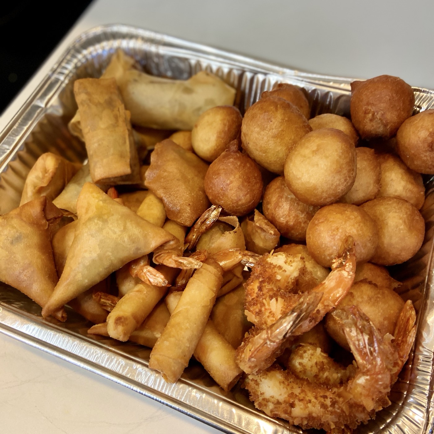 A generous small-chops tray — samosas, spring rolls, golden puff puff and battered shrimp